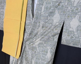 Op de afbeelding: Een vintage kimono met een crèmekleurige achtergrond en een herhalend patroon van gestileerde vazen in grijstinten en groen. Een felgele sjerp is over de kimono gedrapeerd. Het kledingstuk wordt op een houten hanger gepresenteerd.