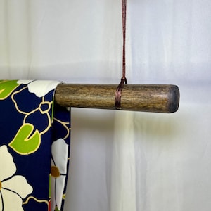 May include: A dark brown wooden rod with a maroon cord attached to the top. A blue and white fabric with a floral pattern is hanging from the rod.