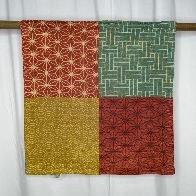 May include: A patterned textile with a geometric design. The fabric is divided into four sections, each with a different pattern in red, green, and gold. The designs include starbursts, woven lines, and wave-like shapes.