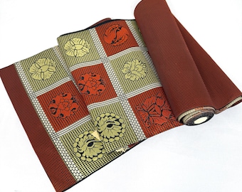 May include: A rolled-up textile with a repeating floral pattern in squares. The squares alternate between yellow and orange flowers on a white grid. The border and rolled section are a solid dark red.