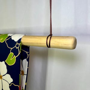 May include: A wooden dowel rod with a brown cord tied around it. The cord is hanging from the ceiling and a fabric with a floral pattern is draped over the rod.