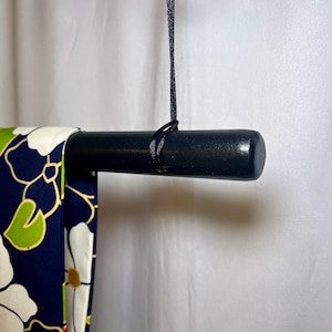 May include: A black wooden rod with a black cord hanging from it. The rod is used to hang fabric, such as a kimono.
