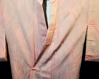 Könnte beinhalten: Ein rosa Seidenkimono mit einem weißen geometrischen Muster. Der Kimono ist gefaltet und auf einem schwarzen Hintergrund ausgestellt.