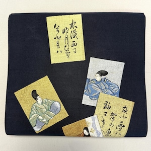 May include: A dark navy blue textile with four decorative cards. The cards feature illustrations of figures in traditional Japanese attire and calligraphy. The cards are gold and silver with black ink.
