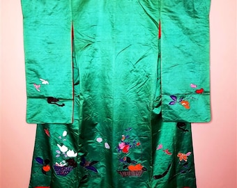 May include: A green silk kimono with embroidered floral designs and a red trim. The kimono features a basket of fruit and flowers, birds, and other floral motifs.