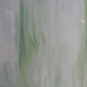 May include: A square piece of green and white stained glass with a streaky pattern. The glass is on a black metal stand.