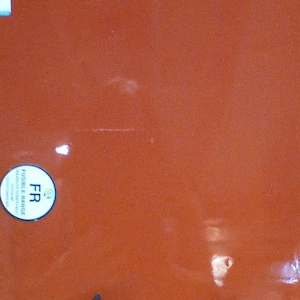 May include: A large, square, orange-red glass sheet with two black star-shaped supports. The glass has a glossy finish and two stickers on the upper left and lower left. The lower sticker reads "FR Fusible Range".