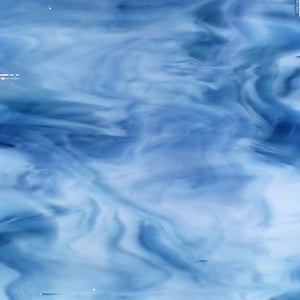 May include: A square piece of stained glass with a swirling pattern of light and dark blue. The glass has a translucent quality, with the colors blending together to create a cloudy effect. The glass is likely used for decorative purposes.