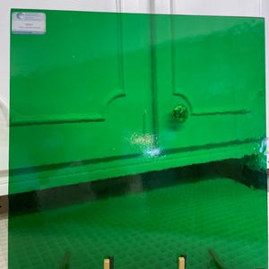 May include: A green glass sheet with a textured surface. The glass sheet is on a white stand with a gold metal base.