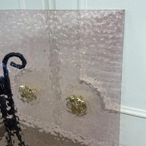 May include: A close-up of a textured, frosted glass panel with two gold-toned metal knobs. The glass has a subtle pink hue.