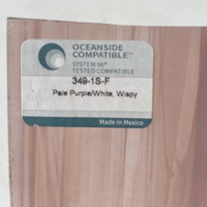 May include: A close-up of a piece of glass with a label. The label reads "OCEANSIDE COMPATIBLE", "SYSTEM 96 TESTED COMPATIBLE", "349-1S-F", and "Pale Purple/White, Wispy". The bottom of the label says "Made In Mexico".