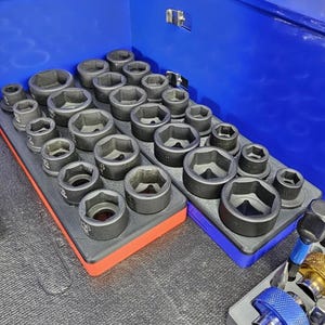 May include: A collection of black sockets of various sizes, neatly arranged on red and blue trays. The sockets are in a blue toolbox, ready for use. The image showcases a well-organized set of tools.