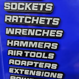 May include: A blue surface with labels for various tools. The labels are black with white lettering and include "Pliers", "Sockets", "Ratchets", "Wrenches", "Hammers", "Air Tools", "Adapters", "Extensions", "Power Tools", and "Screwdrivers".