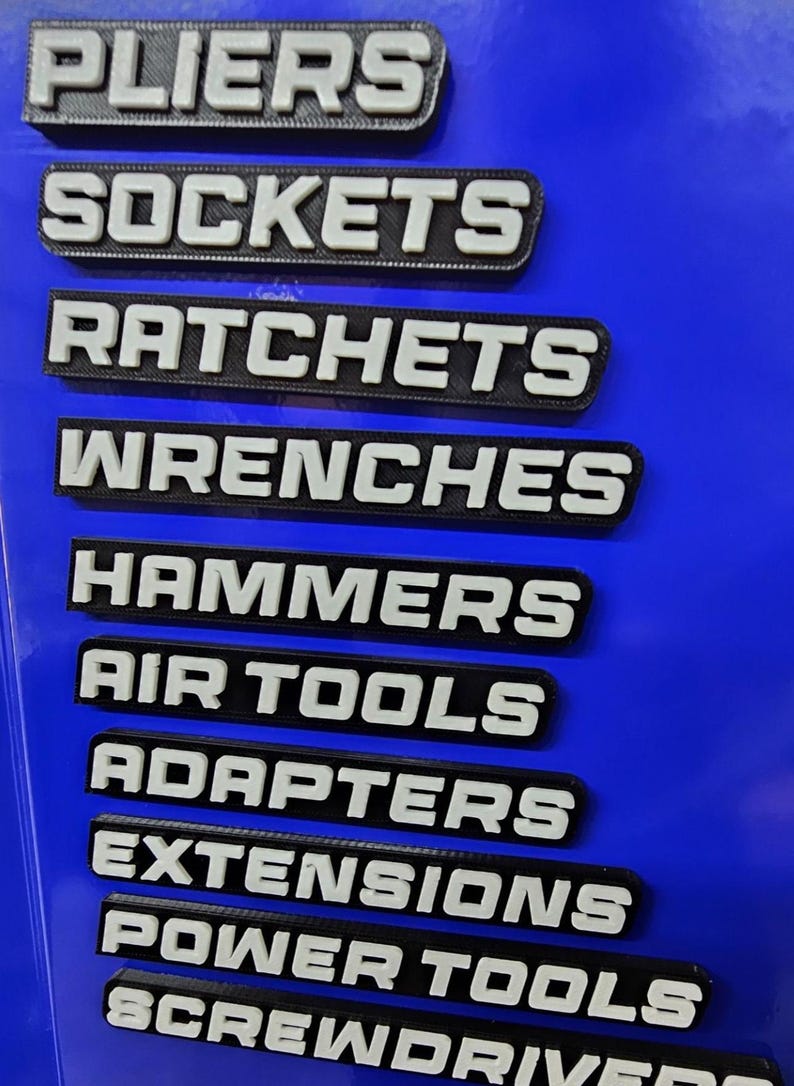 May include: A blue surface with labels for various tools. The labels are black with white lettering and include "Pliers", "Sockets", "Ratchets", "Wrenches", "Hammers", "Air Tools", "Adapters", "Extensions", "Power Tools", and "Screwdrivers".