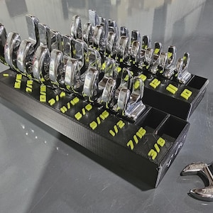 May include: A set of chrome wrenches neatly arranged in a black organizer with yellow size labels. The wrenches are of various sizes, from 3/8 to 1 inch. The organizer is on a gray surface.