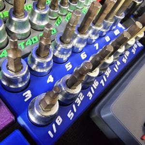May include: Close-up of a set of hex bit sockets in a blue holder. The sockets are arranged in a row and are labeled with sizes such as 1/8, 5/32, and 3/16. The tools are for mechanical work.