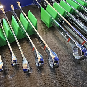May include: A set of chrome combination wrenches, neatly organized in a green holder. The wrenches are arranged by size, with red markings. The image showcases a collection of tools, ideal for automotive or mechanical work.