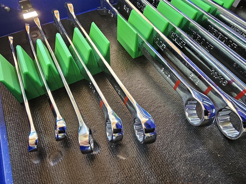 May include: A set of chrome combination wrenches, neatly organized in a green holder. The wrenches are arranged by size, with red markings. The image showcases a collection of tools, ideal for automotive or mechanical work.