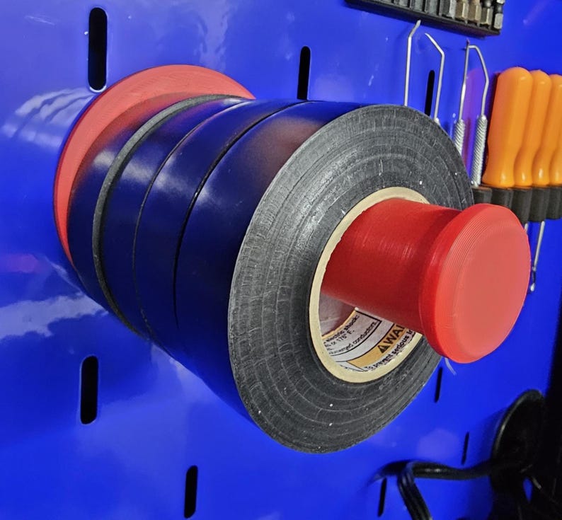 May include: A collection of electrical tape rolls in black, blue, and red, mounted on a blue surface. The tape is held together by a red plastic holder. The image showcases a practical storage solution for electrical supplies.