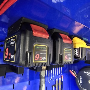 May include: Black and red 20V 9.0Ah high-capacity battery packs and a yellow 8Ah battery pack mounted on a blue surface. The batteries are labeled with the brand name and specifications. The image shows a tool storage setup.