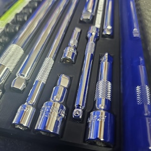 May include: A set of chrome-plated steel socket extensions and adapters arranged in a black foam organizer tray. The tools feature knurled grip sections and are housed within a blue storage case. Each piece is polished with a reflective finish.