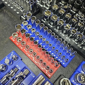 May include: A collection of chrome sockets and ratchets, organized on red, blue, and black trays. The sockets are arranged by size, with measurements in inches. The image showcases a variety of tools for automotive or mechanical work.