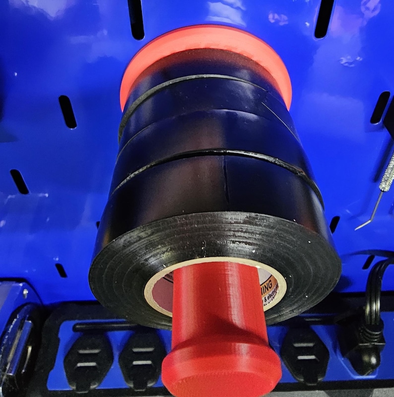 May include: A red and black electrical tape dispenser. The dispenser holds several rolls of black electrical tape. The tape is stacked on a red, cylindrical holder. The dispenser is mounted on a blue surface.