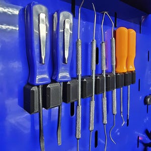May include: A collection of tools, including screwdrivers and dental picks, organized on a blue pegboard. The screwdrivers have blue handles and silver blades, while the picks have silver handles and curved tips. Orange-handled tools are also present.