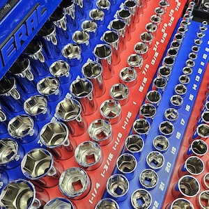 May include: A close-up of a tool set with various chrome sockets arranged on red and blue trays. The sockets are labeled with sizes, including 1-5/16, 1-1/4, and 1-3/16 inches. The word "ERAL" is visible on the blue tray.