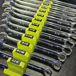May include: A set of chrome wrenches with yellow holders, arranged in a row. Each wrench has a different size, indicated by black text on the yellow holders. The wrenches are on a dark surface.