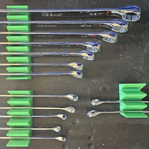 May include: A collection of chrome wrenches of various sizes, neatly organized in green holders. The wrenches are arranged in rows, showcasing their different dimensions. The image highlights the tools' shiny surfaces and the organized storage system.