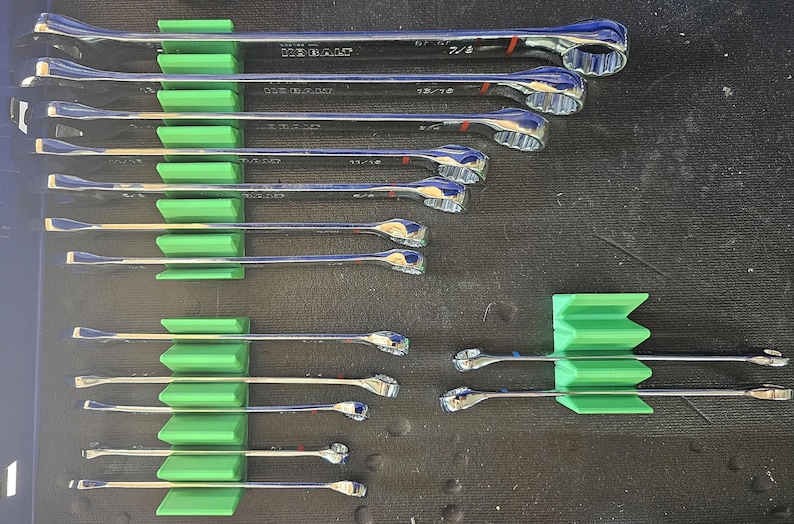 May include: A collection of chrome wrenches of various sizes, neatly organized in green holders. The wrenches are arranged in rows, showcasing their different dimensions. The image highlights the tools' shiny surfaces and the organized storage system.