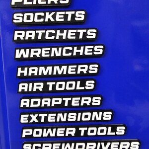 May include: Black and white tool labels with the following text: PLIERS, SOCKETS, RATCHETS, WRENCHES, HAMMERS, AIR TOOLS, ADAPTERS, EXTENSIONS, POWER TOOLS, and SCREWDRIVERS. The labels are on a blue surface.