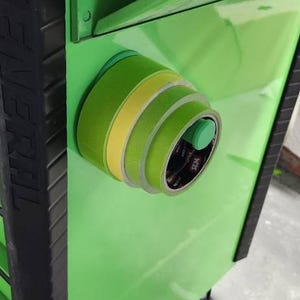May include: A close-up of a green tool cabinet with rolls of green and yellow masking tape attached to the side. The tape is held in place by a magnetic holder. The cabinet is a bright, glossy green.