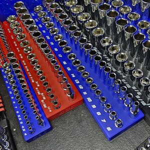 May include: Organized set of chrome sockets in various sizes, neatly arranged on red, blue, and black trays. The sockets are labeled with inch measurements, providing a clear view of the tools. The image showcases a well-organized tool collection.