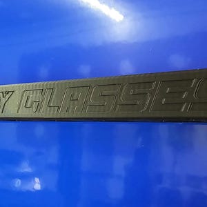 May include: A black rectangular object with the words "SAFETY GLASSES" embossed on it. The object is set against a blue background.