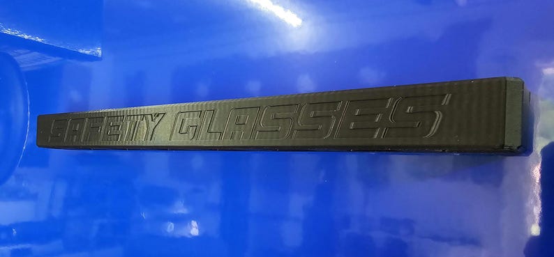 May include: A black rectangular object with the words "SAFETY GLASSES" embossed on it. The object is set against a blue background.