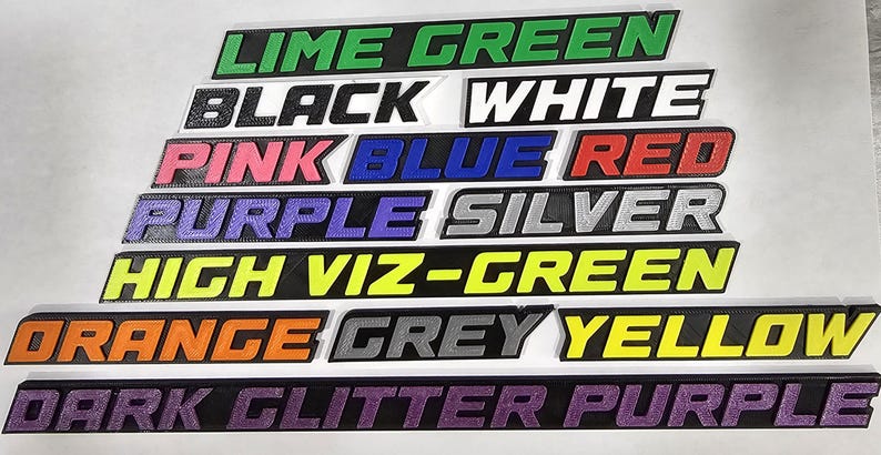 May include: A collection of rectangular signs in various colors, each displaying a different color name in bold, sans-serif font. Colors include lime green, black, white, pink, blue, red, purple, silver, high viz-green, orange, grey, yellow, and dark glitter purple.