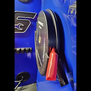 May include: A black and silver Maddox tool holder with a red clamp and a black clamp. The tool holder is mounted on a blue surface. The Maddox logo is visible on the tool holder.
