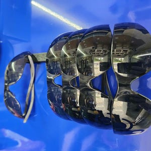 May include: A display of several pairs of mirrored sunglasses with a unique, curved design. The sunglasses are arranged on a blue surface, reflecting the surrounding environment. The frames are a shiny, metallic color.
