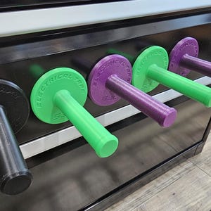 May include: A row of colorful electrical tape holders. The holders are black, green, and purple, with the words "ELECTRICAL TAPE" printed on the circular tops. The handles are cylindrical and extend outward.