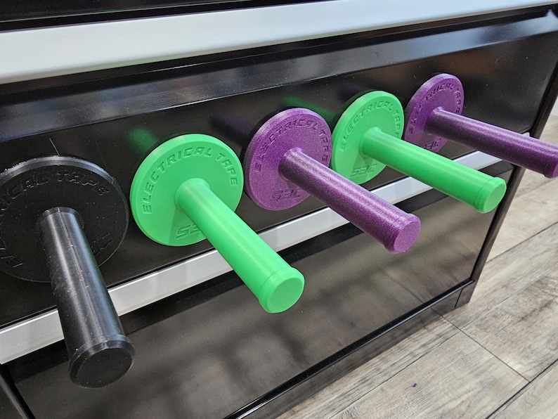 May include: A row of colorful electrical tape holders. The holders are black, green, and purple, with the words "ELECTRICAL TAPE" printed on the circular tops. The handles are cylindrical and extend outward.