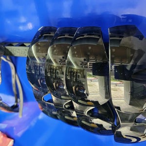 May include: Black sunglasses with a reflective surface. The sunglasses have a unique, curved design with a thick frame and a bridge. The lenses are dark, and the arms are thin and gray. The sunglasses are set against a blue background.