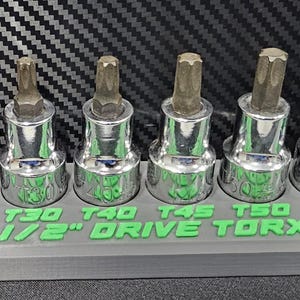 May include: A set of Torx bit sockets in a gray holder. The sockets are chrome with brown tips, labeled T20 to T70. The holder is labeled "1/2" DRIVE TORX" in green.