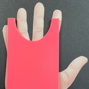 May include: A bright pink plastic hand-shaped mold with a cutout for a hand. The mold is designed to create a hand-shaped object.