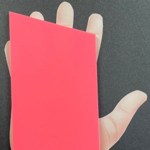 May include: A bright pink rectangular piece of paper held in a hand.