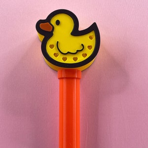 May include: A yellow rubber duck toy with black outlines and a red beak, attached to a bright orange plastic stick.