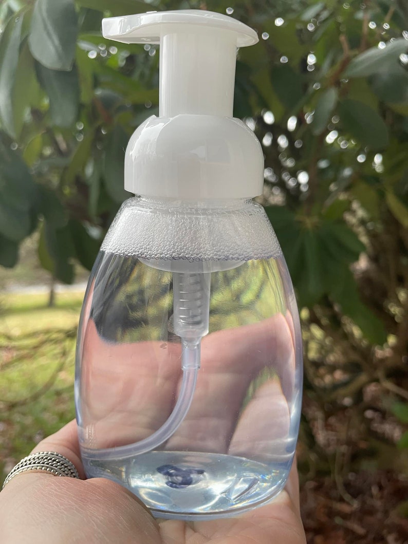 May include: A clear plastic bottle with a white pump dispenser filled with a clear liquid. The bottle is in a hand.