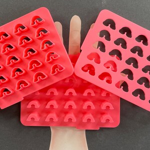May include: Three pink plastic molds for making rainbow-shaped treats. Each mold has a grid of small rainbow-shaped cutouts.