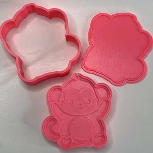 May include: Three pink plastic cookie cutters shaped like a monkey, a paw print, and a blank circle.